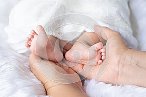 Mother Hand hold Cute newborn foot baby girl in white blanket onÂ nurseryÂ bed.Adorable new born child people